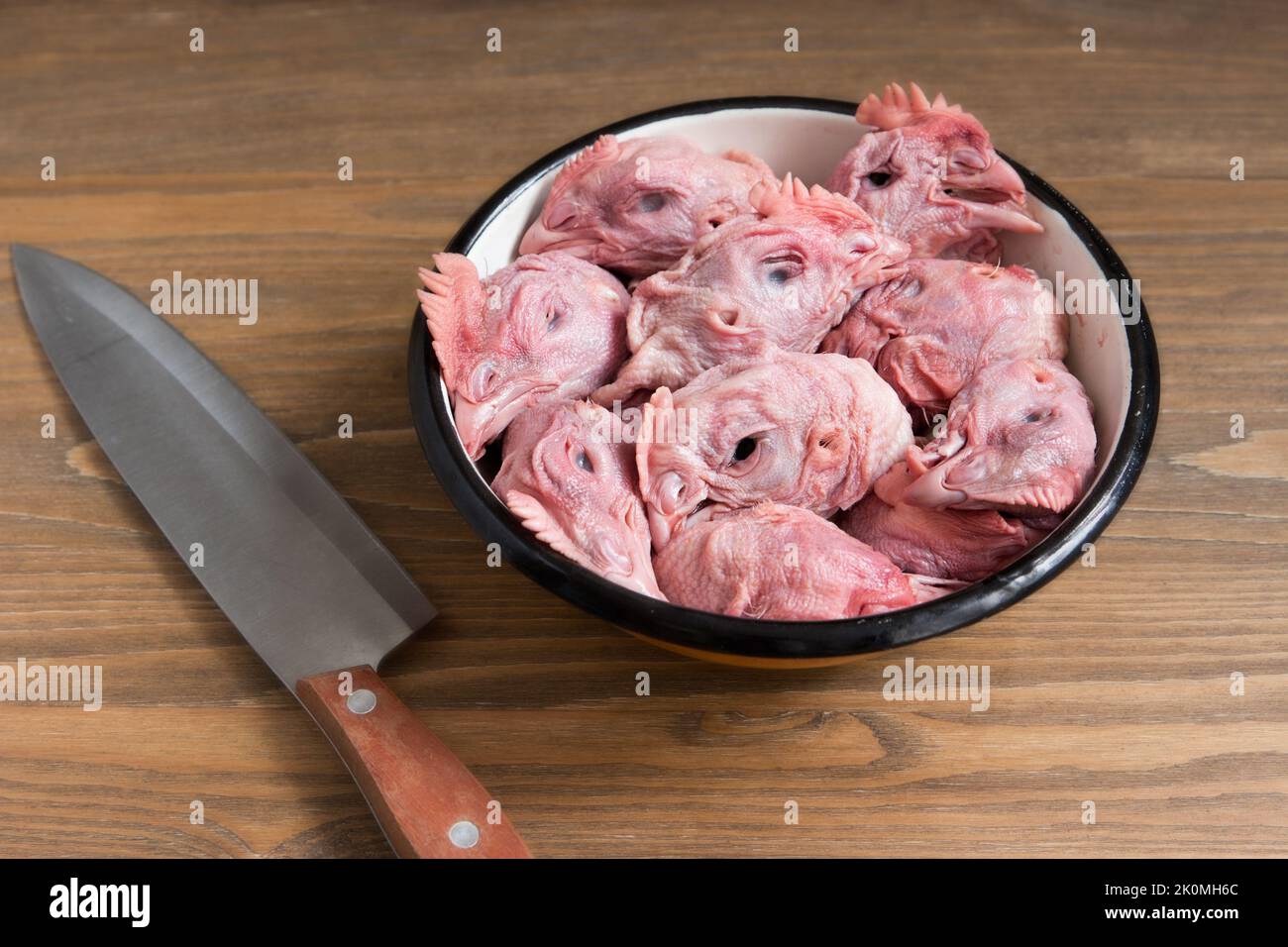 Des têtes de poulet crues dans un plat en métal et un gros couteau Banque D'Images