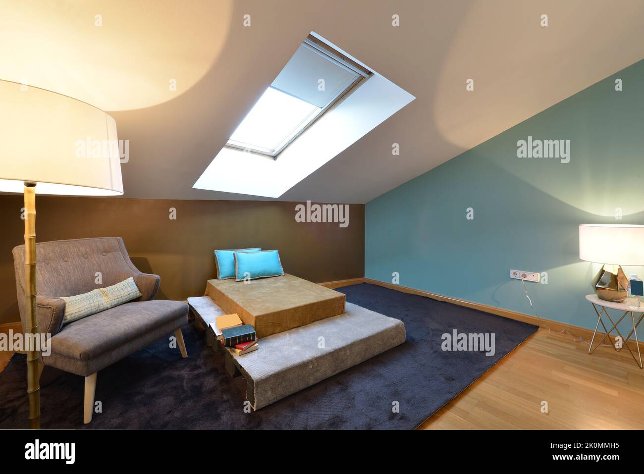 Coin lecture de la chambre avec chaise à dossier sous la lampe, tapis de cerf foncé et divan sous la lucarne au plafond incliné Banque D'Images