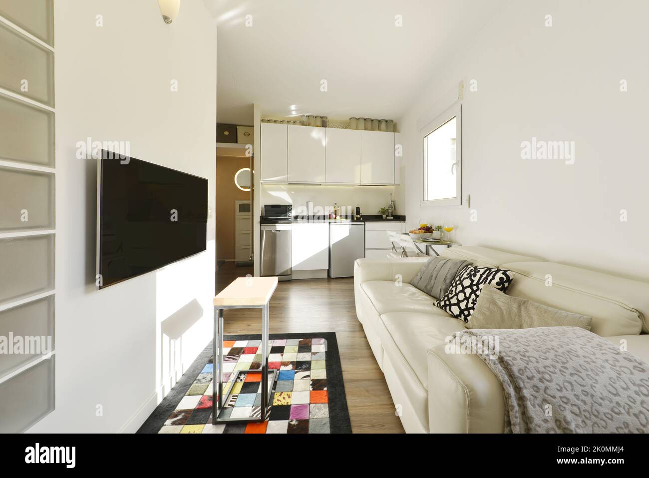 Salon-studio avec canapé en cuir blanc, cuisine américaine, décoration claire et chambre à coucher en arrière-plan Banque D'Images