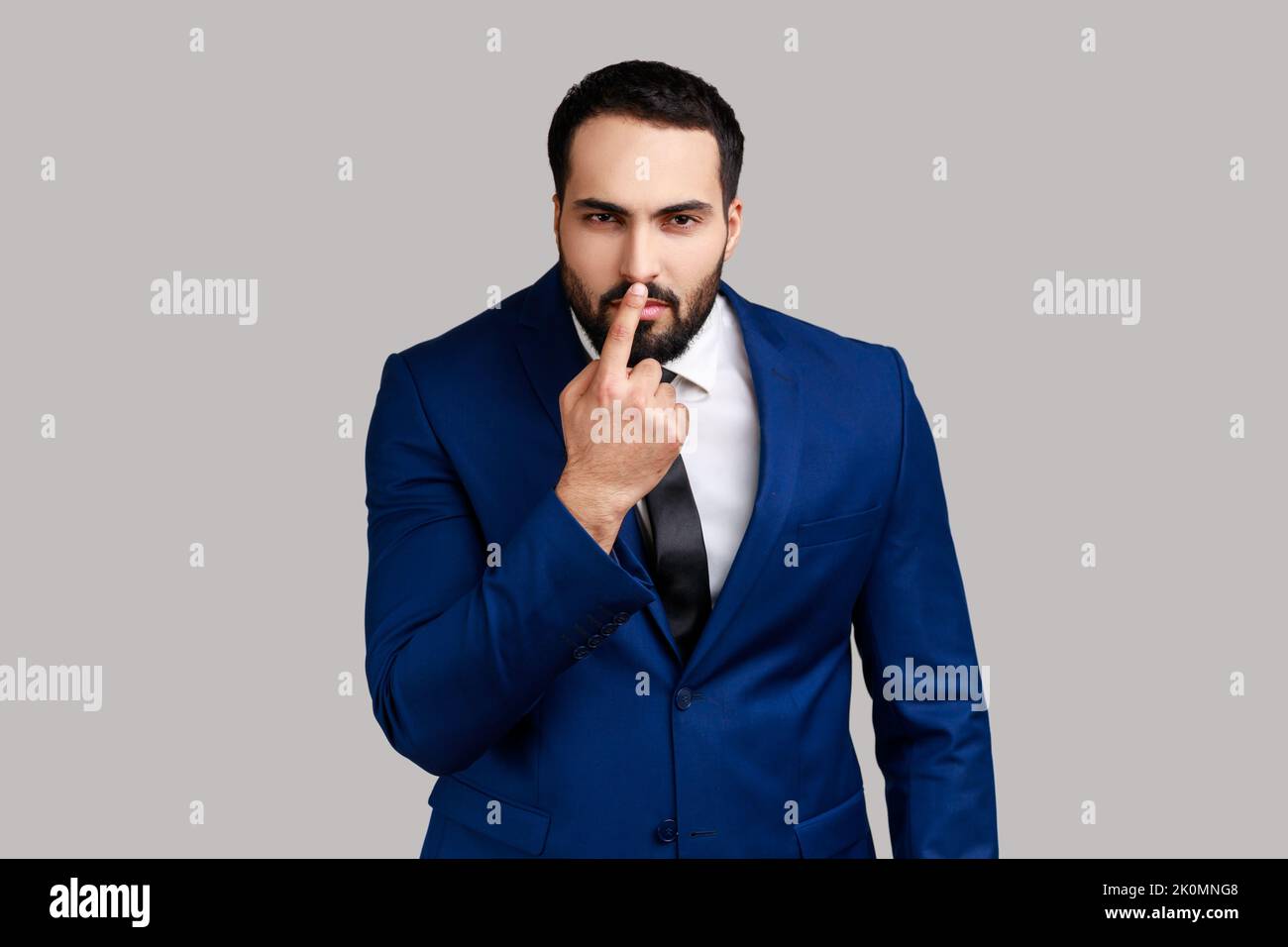 Homme barbu regardant avec le regard suspect incrédule et touchant le nez, vous faisant gesturer est menteur, suspectant le mensonge, portant le costume officiel de style. Prise de vue en studio isolée sur fond gris. Banque D'Images