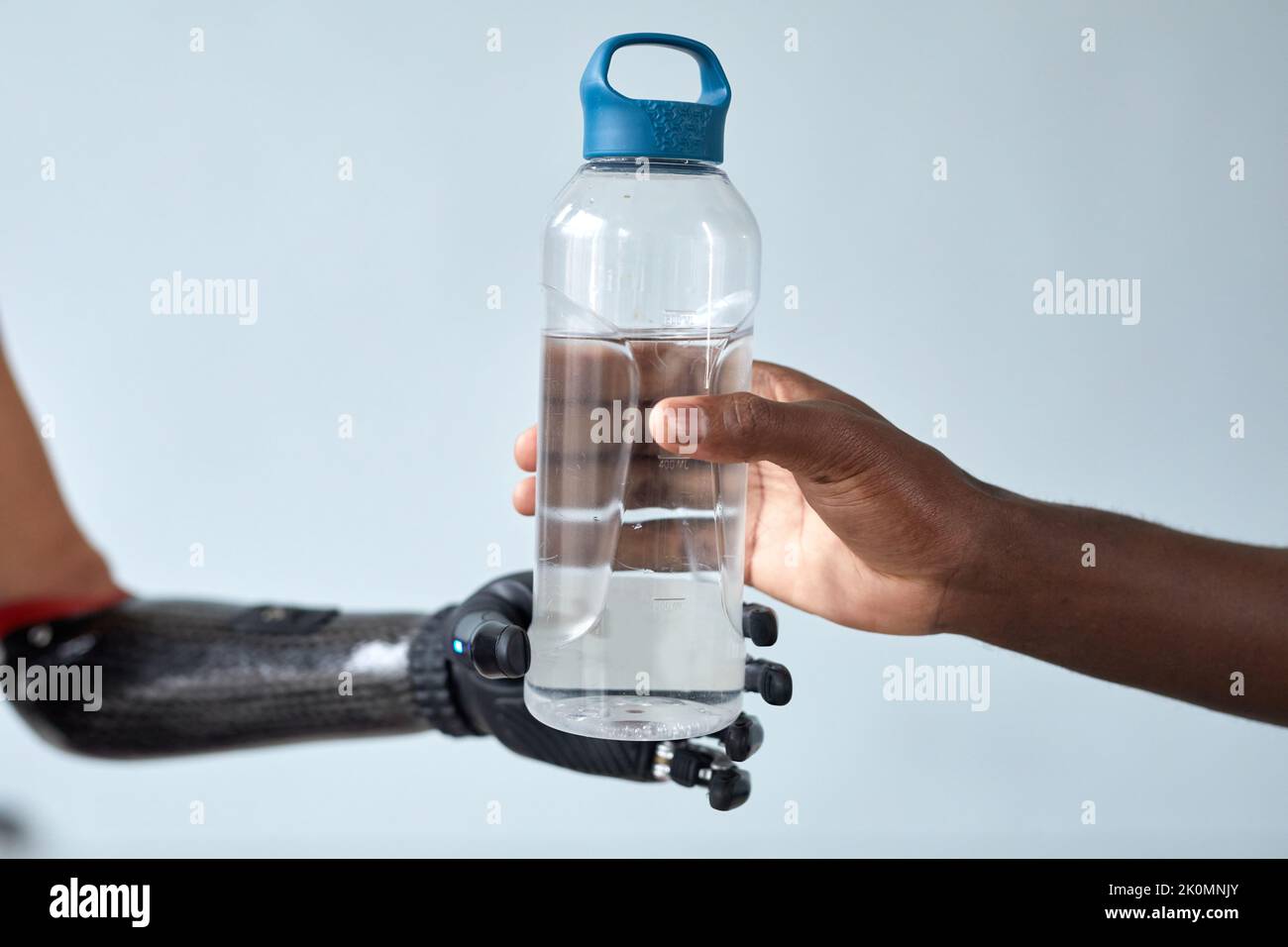 Gros plan de l'homme africain donnant une bouteille d'eau à une femme avec un bras prothétique isolé sur fond bleu Banque D'Images