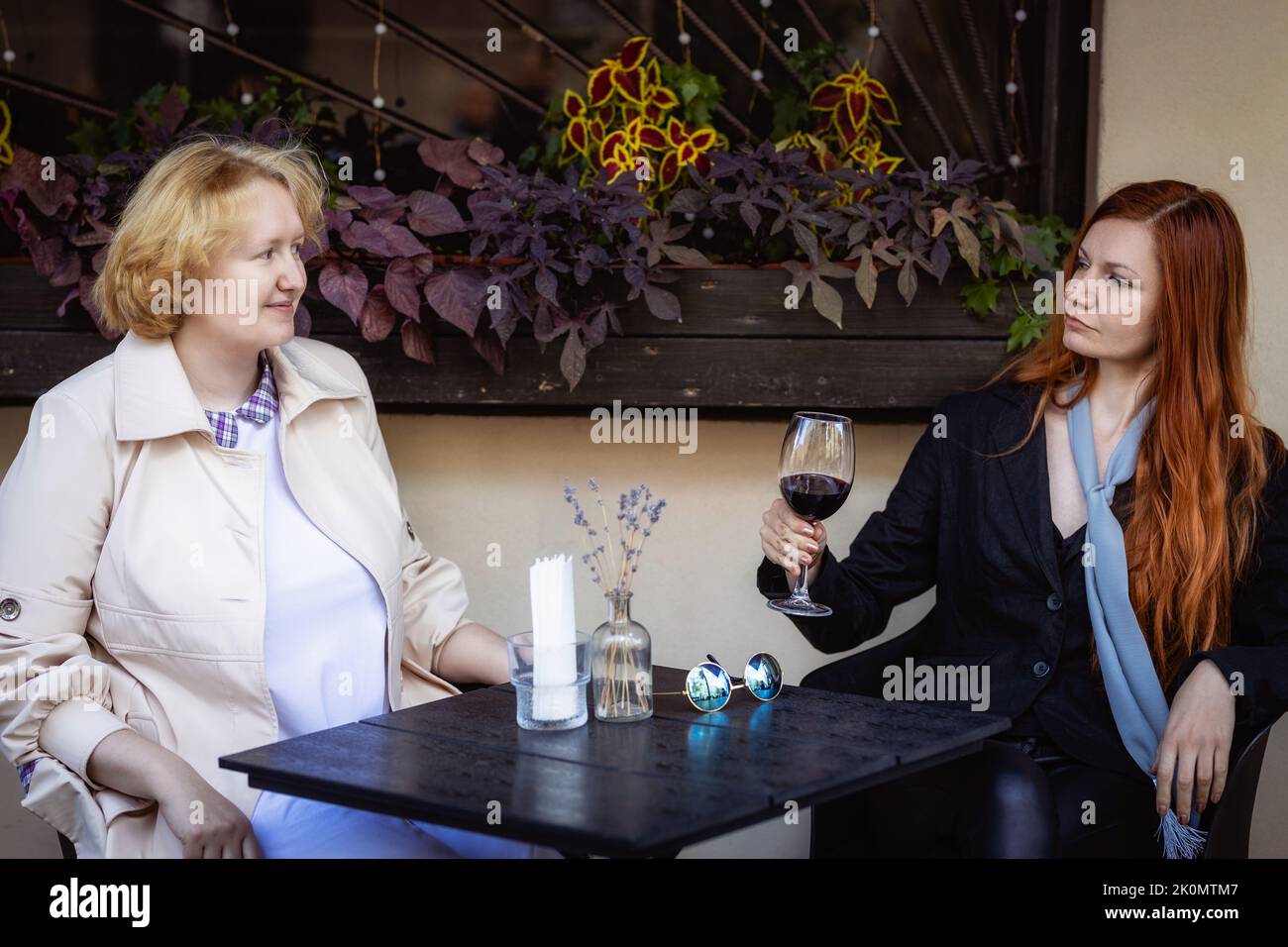 Deux femmes ensemble - blonde dans la lumière et rouge dans les vêtements sombres parlant au bar d'un café de rue. Banque D'Images