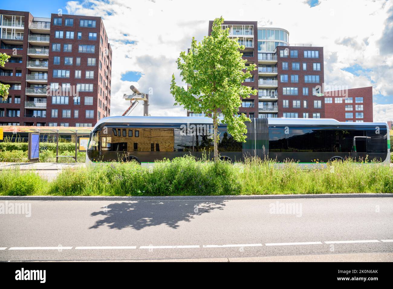 Le bus de ville électrique se recharge à un arrêt de bus dans un quartier résidentiel de banlieue par une belle journée d'été Banque D'Images