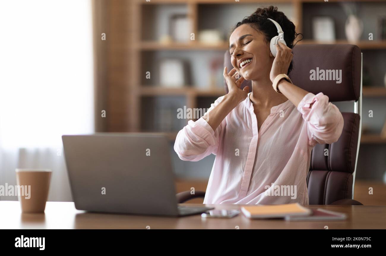 Jeune femme joyeuse écoutant de la musique au bureau Banque D'Images