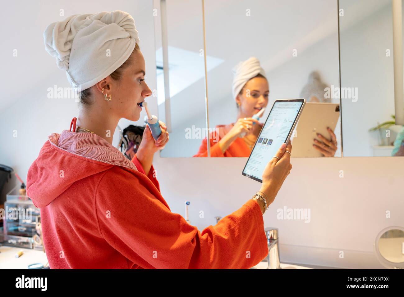 Image symbolique Precrastination, jeune femme essayant de faire beaucoup de choses à la fois, dans la salle de bains, sur l'ordinateur, parler au téléphone, lire les nouvelles Banque D'Images