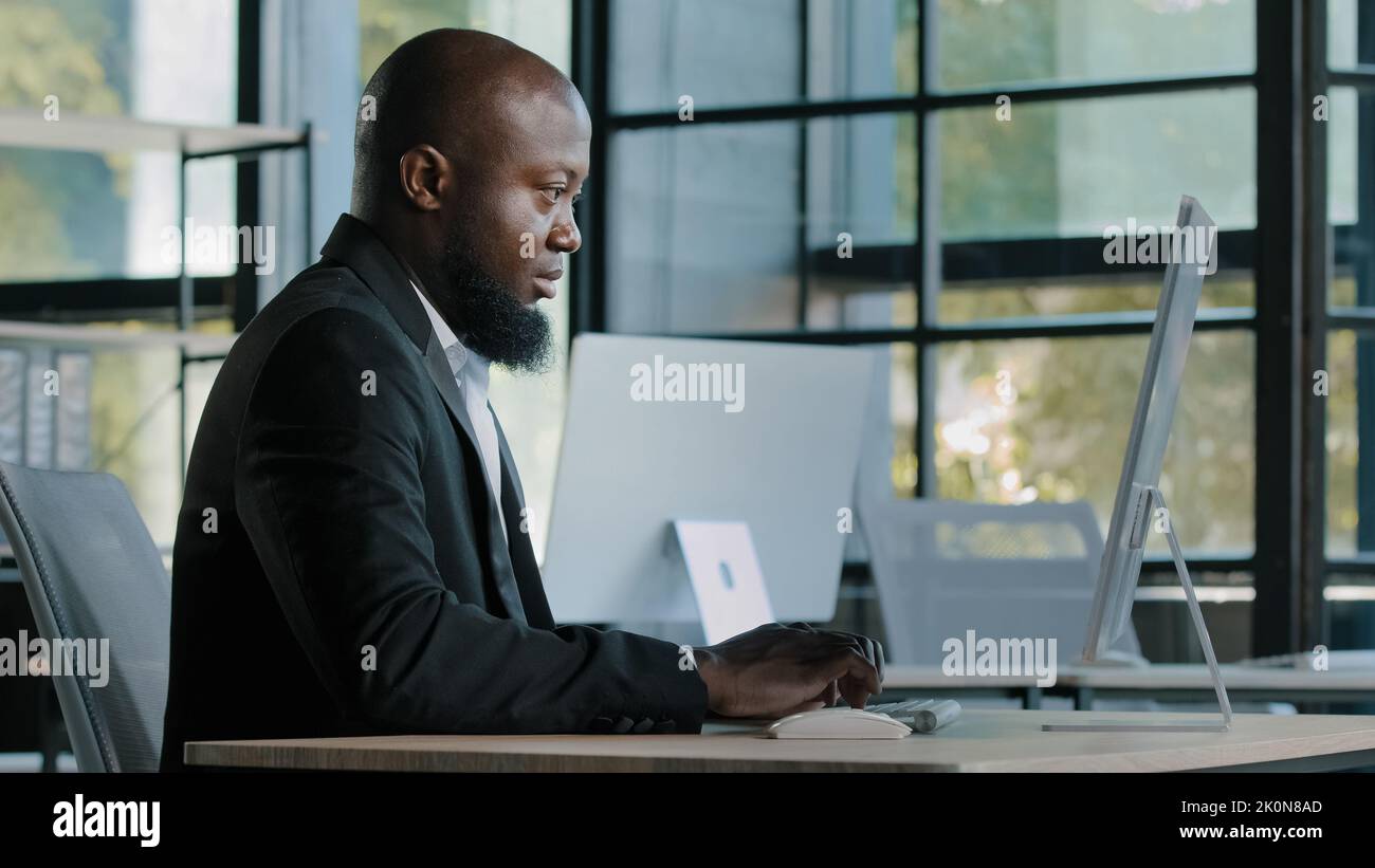 Vue latérale le directeur général de l'analyste d'affaires afro-américain senior s'assoit au bureau en tapant un e-mail discutant sur une recherche concentrée sur l'ordinateur de l'entreprise Banque D'Images
