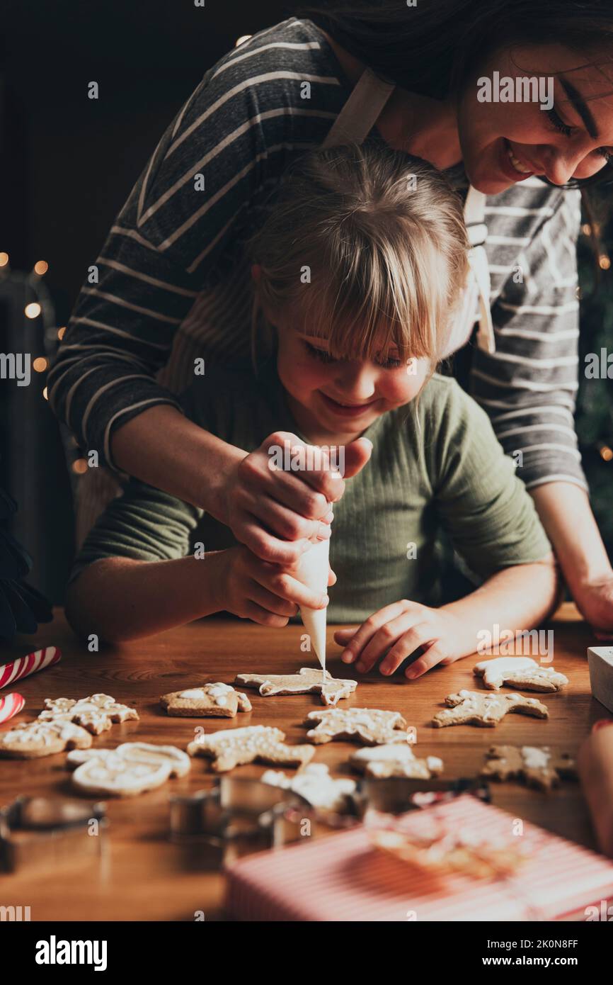 Noël, pain d'épice du nouvel an cuisine, fabrication, décoration de biscuits fraîchement cuits avec du glaçage et du mastic. Momie et enfant, authentiques moments agréables. Maman aidant la petite fille mignonne à décorer le cookie Banque D'Images