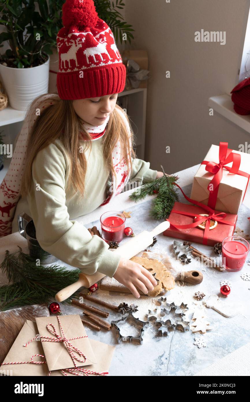 Une fille dans un chapeau rouge de Noël et le sweat à capuche fait des biscuits de pain d'épice.traditionnel Noël fait maison biscuits de pain d'épice, la cannelle et les lettres du nouvel an et boîtes-cadeaux. Banque D'Images