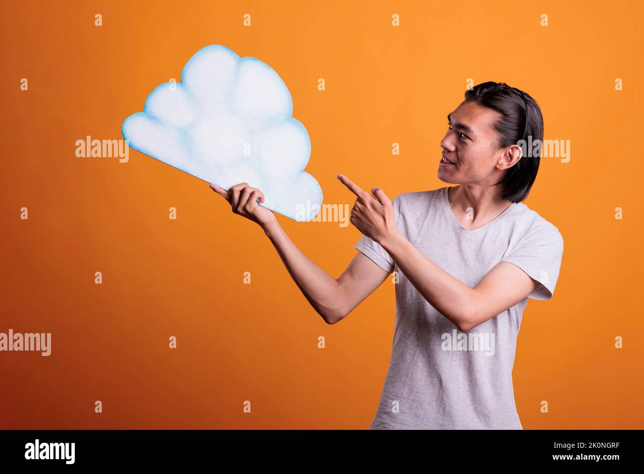Jeune homme asiatique souriant tenant vide blanc nuage forme avec espace de copie, produit publicitaire. Adolescent gai debout, pointant sur la bulle de pensée vide avec un endroit pour le texte Banque D'Images