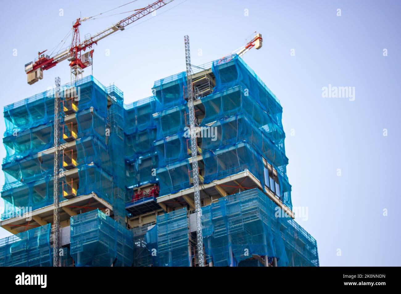 Façade de deux bâtiments à plusieurs étages recouverte de mesh de protection sur fond bleu ciel. Construction de bâtiments résidentiels, rénovation de maisons Banque D'Images