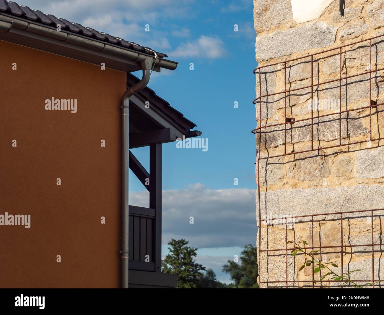Vieux mur avec une grille pour l'escalade des plantes. L'extérieur du bâtiment rénové est éclairé par la lumière du soleil. Un autre bâtiment et un ciel bleu sont en arrière-plan. Banque D'Images