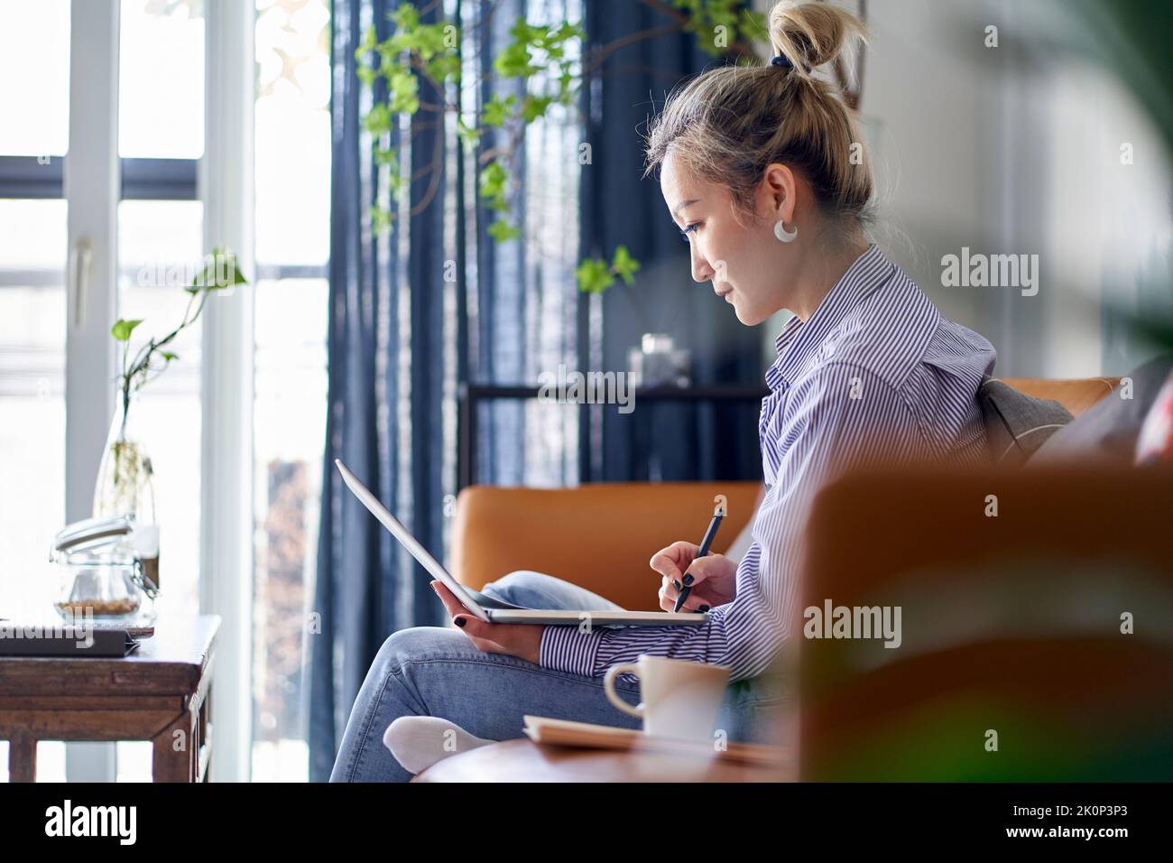 femme asiatique professionnelle mature travaillant sur un document papier de la maison en utilisant un ordinateur portable vue latérale Banque D'Images