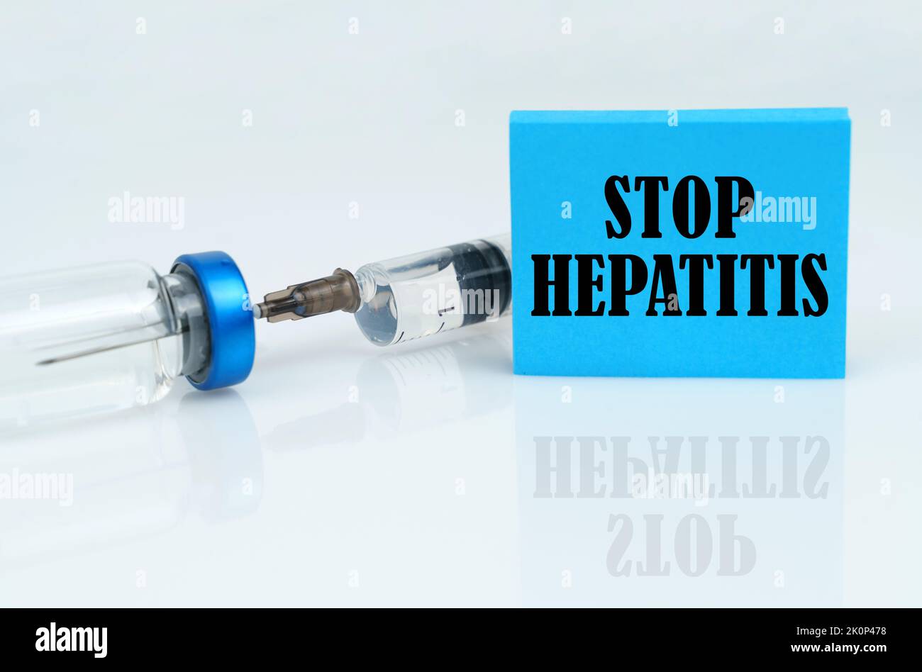Concept médical. Sur une surface réfléchissante blanche, il y a une seringue avec une ampoule et une plaque bleue avec l'inscription - STOP HÉPATITE Banque D'Images