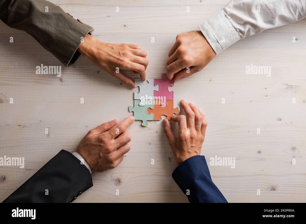 Les mains de quatre hommes d'affaires se joignent à des pièces de puzzle assorties de différentes couleurs pastel sur un fond en bois. Banque D'Images
