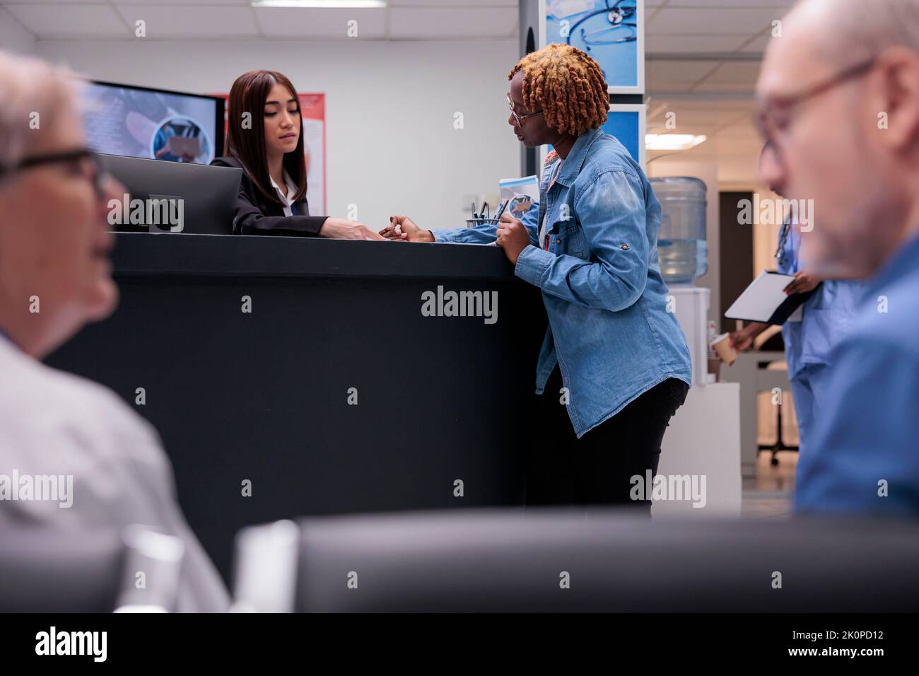 Personne afro-américaine remplissant les dossiers de rapports, parlant à la réceptionniste à la réception de l'hôpital. Une femme qui rédige un formulaire médical avant un rendez-vous avec un médecin au centre de santé. Banque D'Images