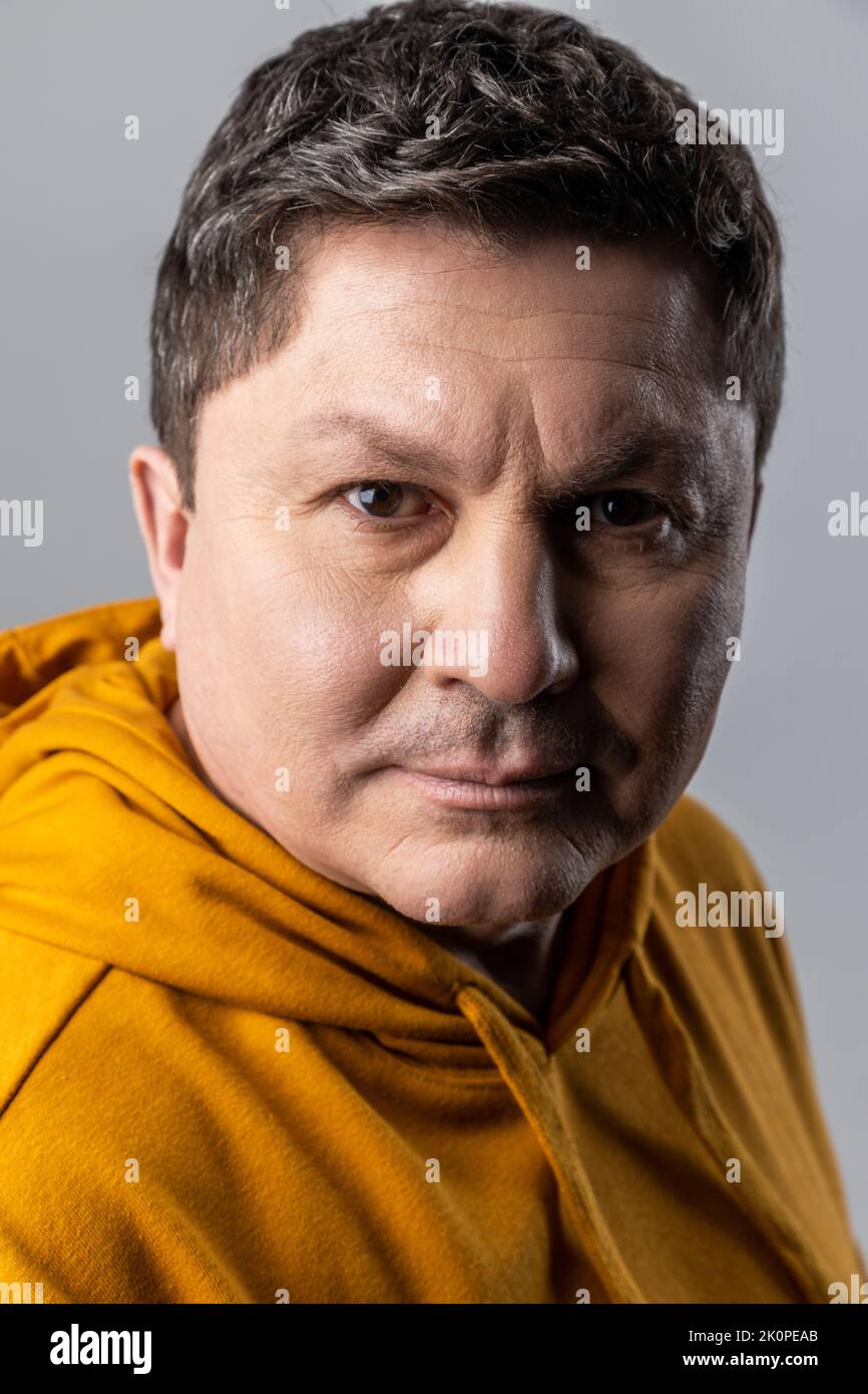 Portrait en gros plan d'un homme élégant et confiant qui regarde l'appareil photo avec une expression calme, des soins de santé et de beauté masculins, portant un sweat à capuche de style urbain. Prise de vue en studio isolée sur fond gris. Banque D'Images