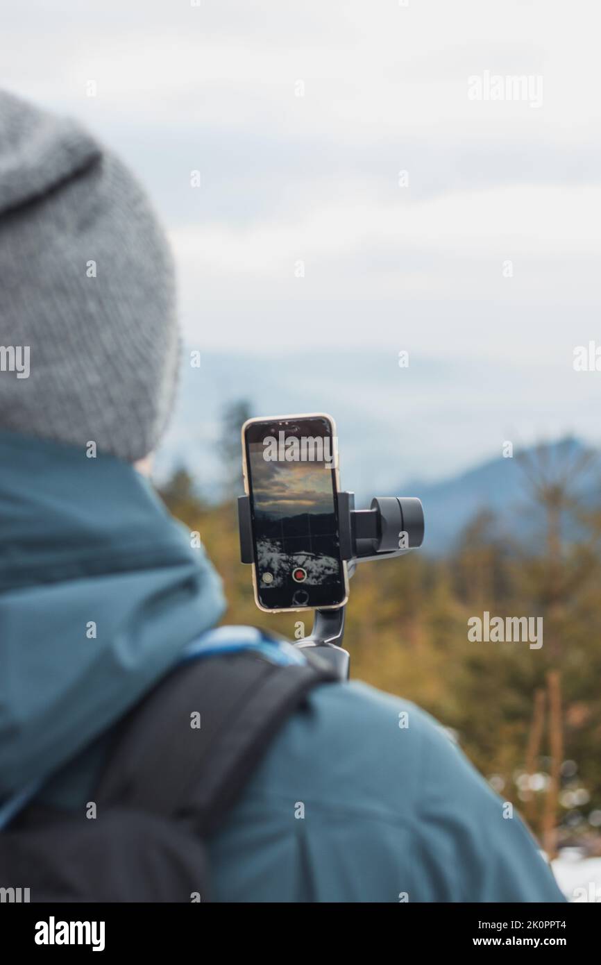 Homme dans les vêtements d'hiver utilise la dernière technologie pour vlog et enregistrer des vidéos. Un homme d'âge moyen filme sur un téléphone portable à travers une nacelle. Banque D'Images