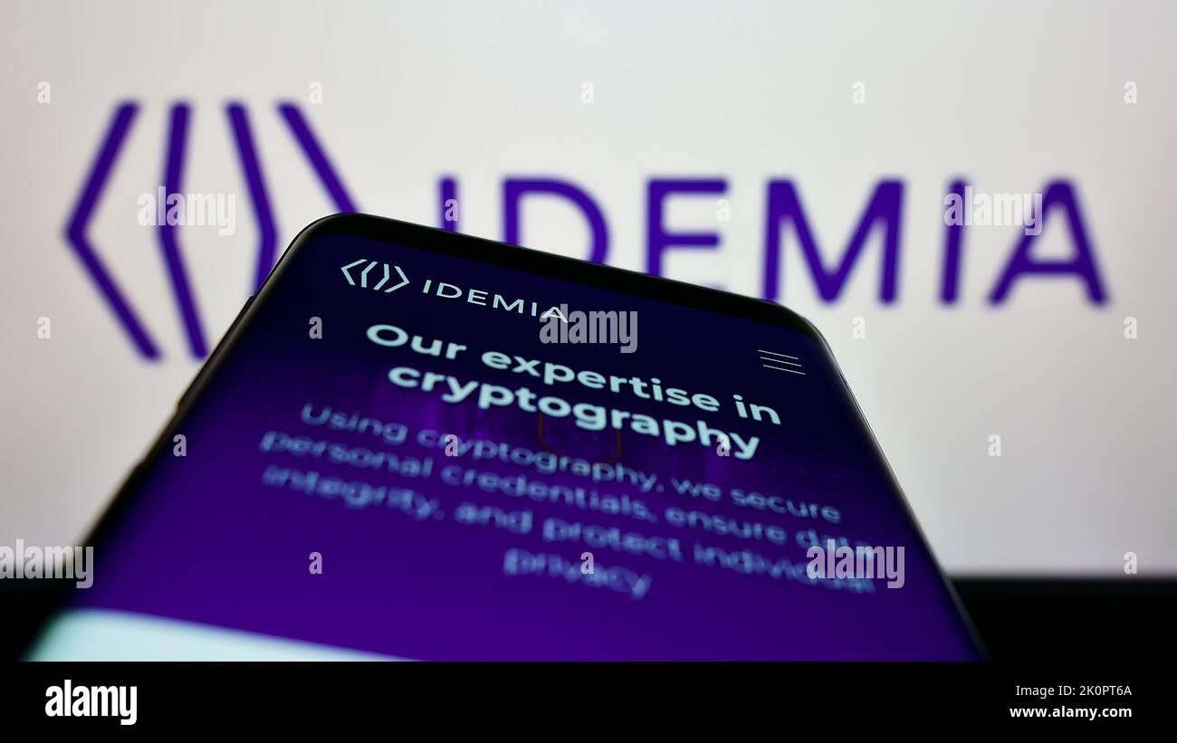 Téléphone mobile avec le site Internet de la société de technologie IDEMIA France SAS à l'écran devant le logo de l'entreprise. Faites la mise au point dans le coin supérieur gauche de l'écran du téléphone. Banque D'Images