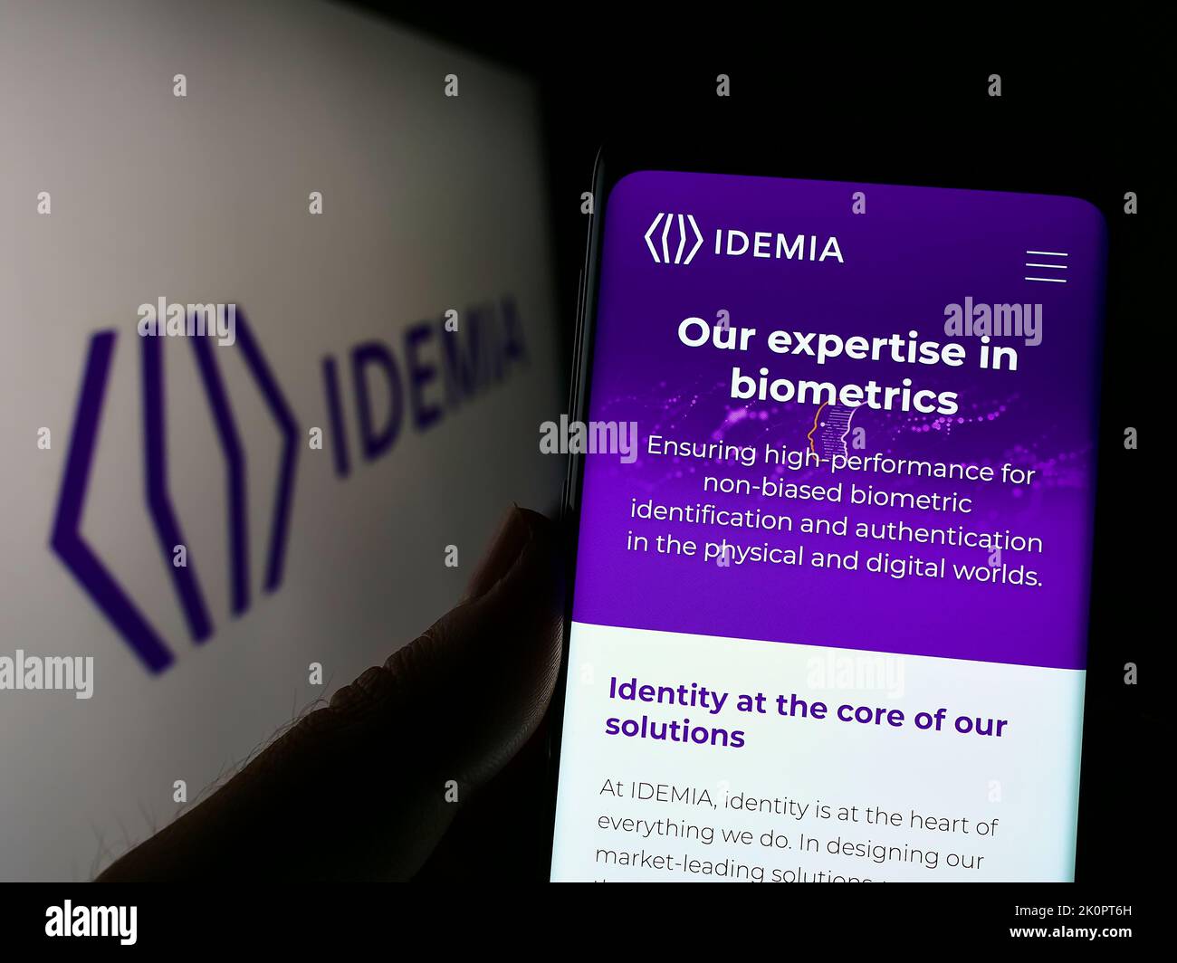 Personne tenant le téléphone portable avec la page web de la société de technologie IDEMIA France SAS sur l'écran devant le logo. Concentrez-vous sur le centre de l'écran du téléphone. Banque D'Images