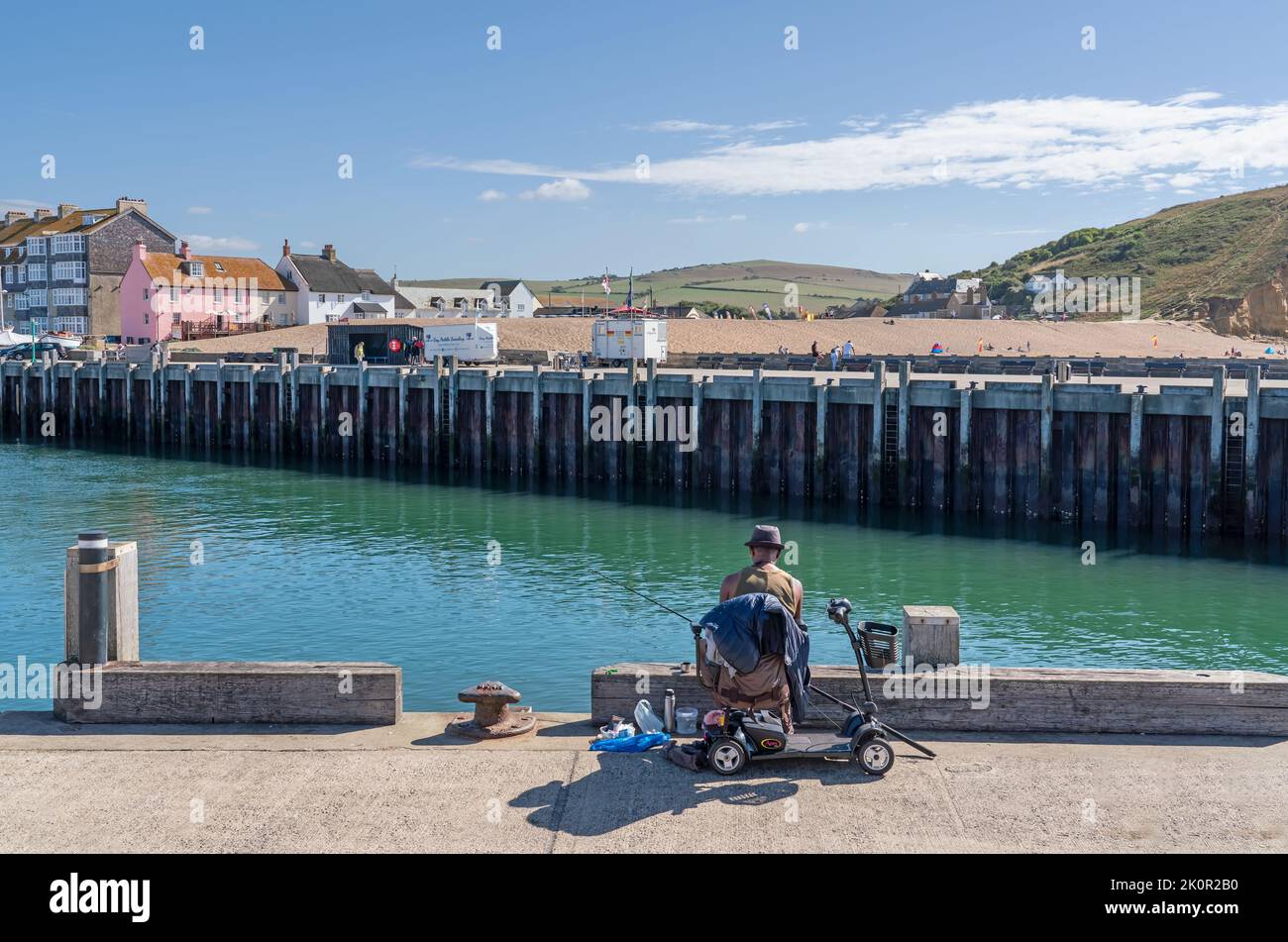 Un homme assis sur un scooter de mobilité tout en pêchant au large du port de West Bay, Dorset. 26th août 2022. Accès aux espaces ouverts et aux loisirs. Banque D'Images