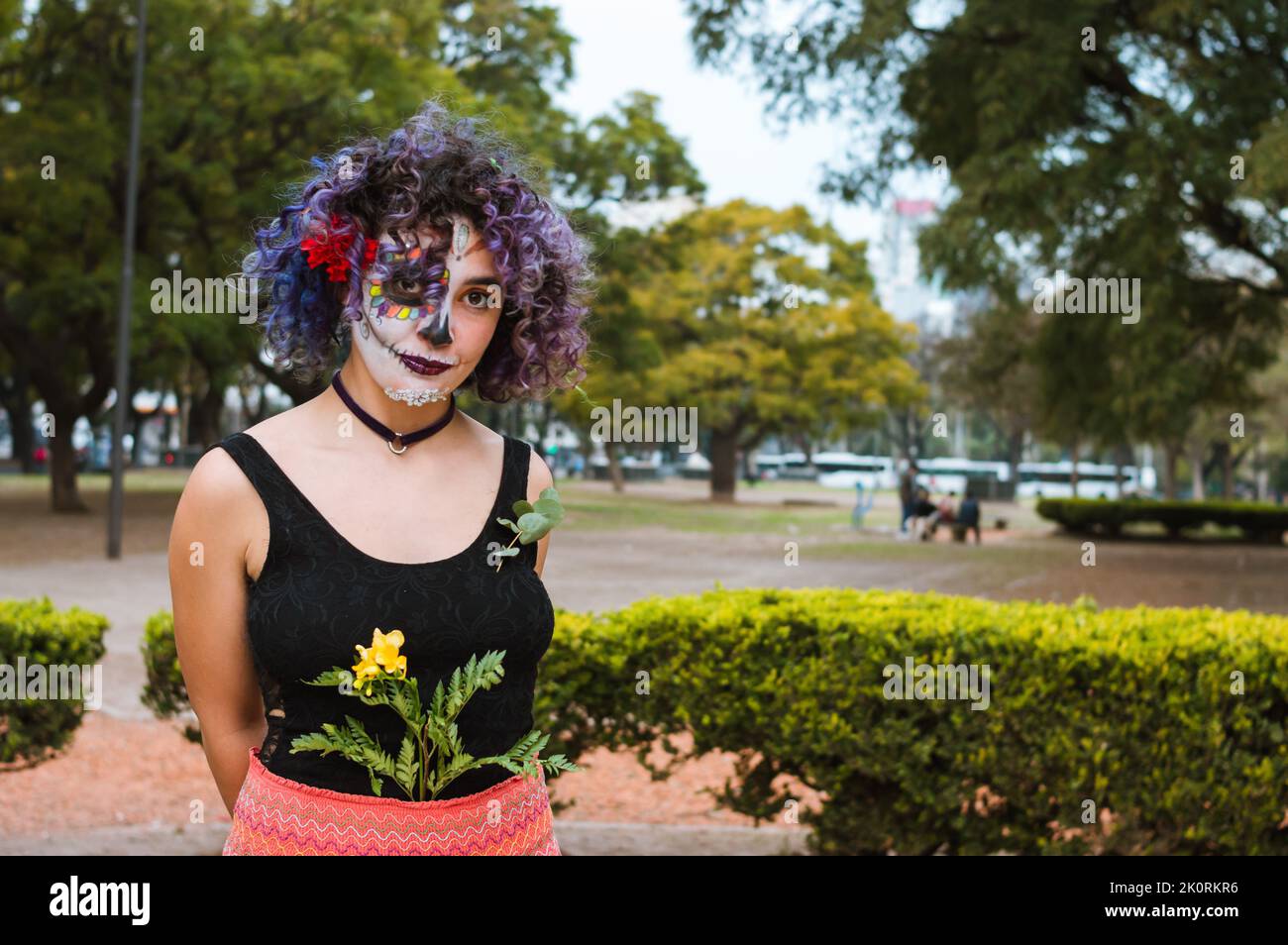 Jeune femme latine caucasienne avec le maquillage de la Calavera Catrina et des vêtements folkloriques, debout dans le parc regardant la caméra avec espace de copie. Banque D'Images