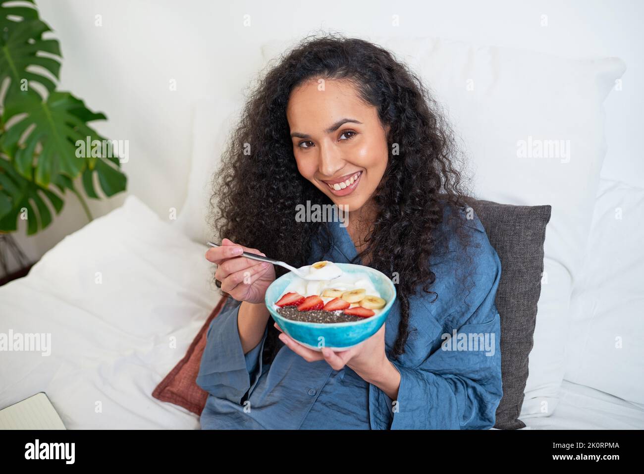 Une belle femme multi-ethnique mange un bol de fruits dans son lit Banque D'Images