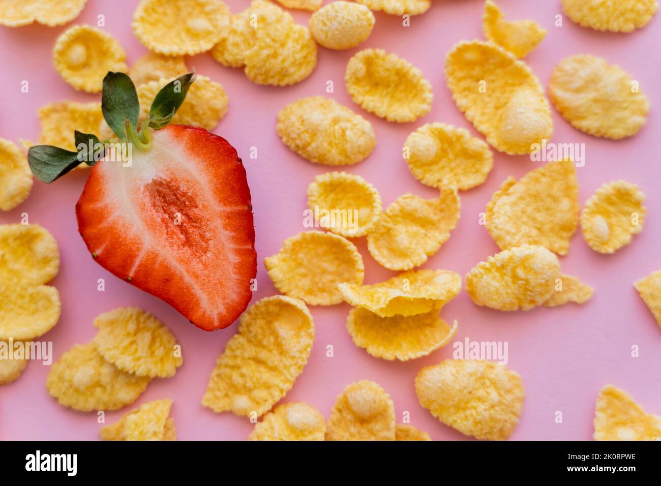 gros plan de fraises coupées fraîches autour de flocons de maïs croustillants sur image rose Banque D'Images