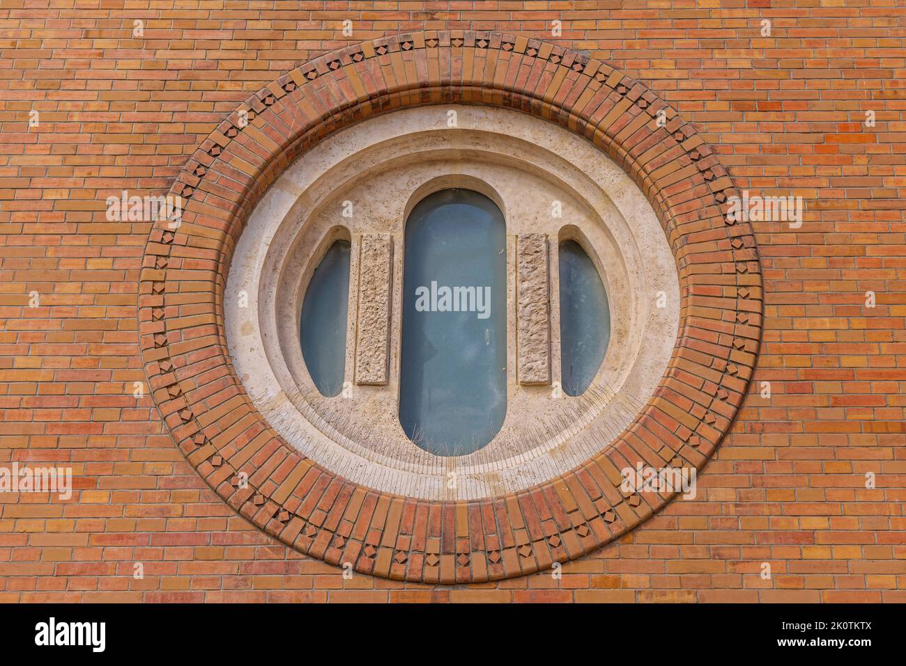 Fenêtre ronde au mur de briques de l'église Votive à Szeged avec des aiguilles de protection d'oiseaux Banque D'Images
