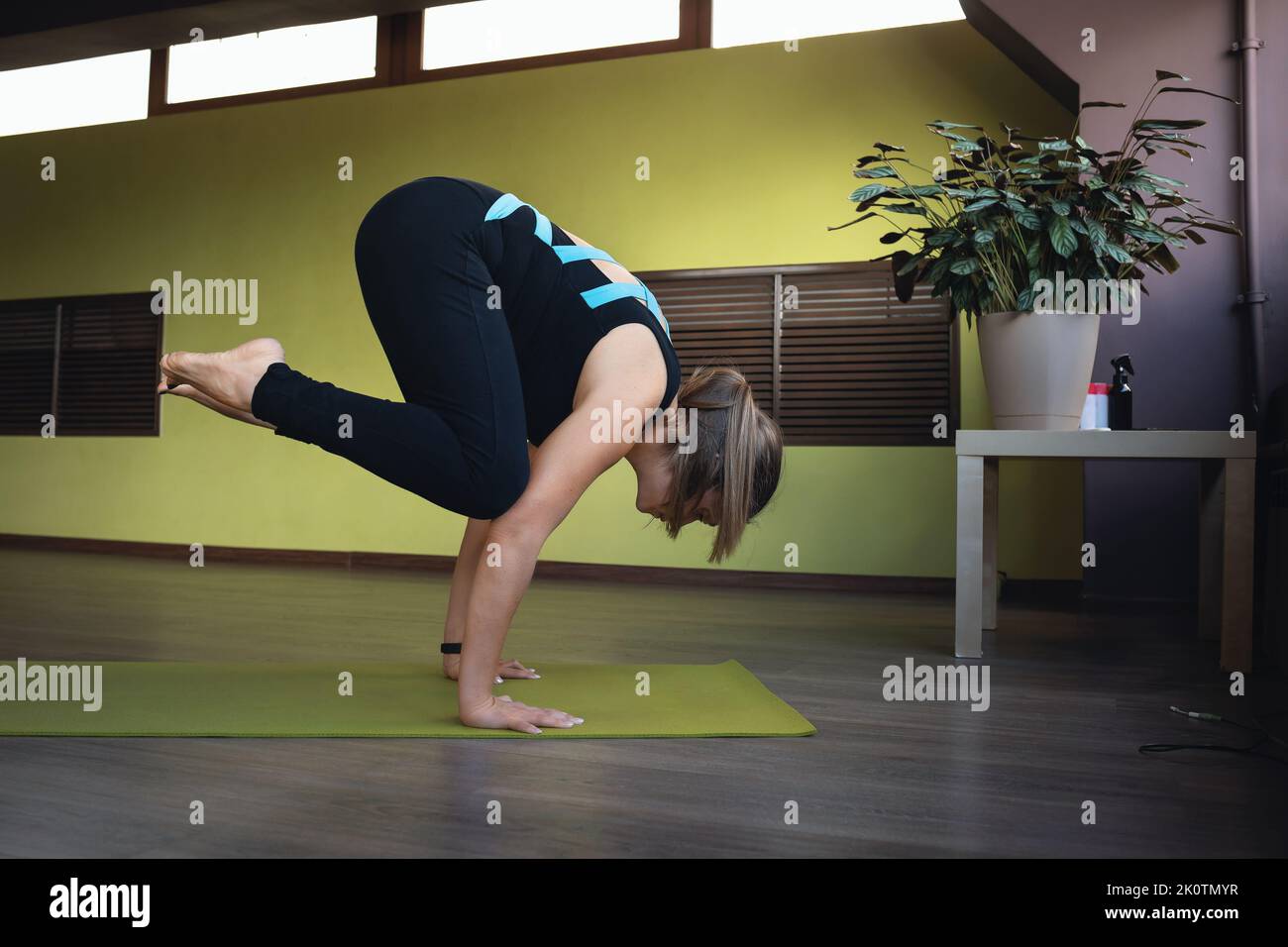 Femme dans les vêtements de sport pratiquant le yoga faisant de l'exercice de bakasana, pose de grue, équilibre de l'asana, s'exerçant sur le tapis en studio Banque D'Images
