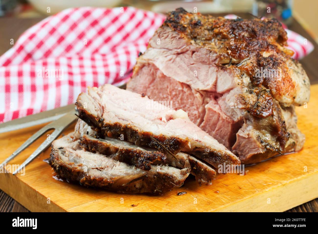 Viande de porc cuite avec épices tranchées sur une planche à découper brune avec couteau et fourchette. Banque D'Images