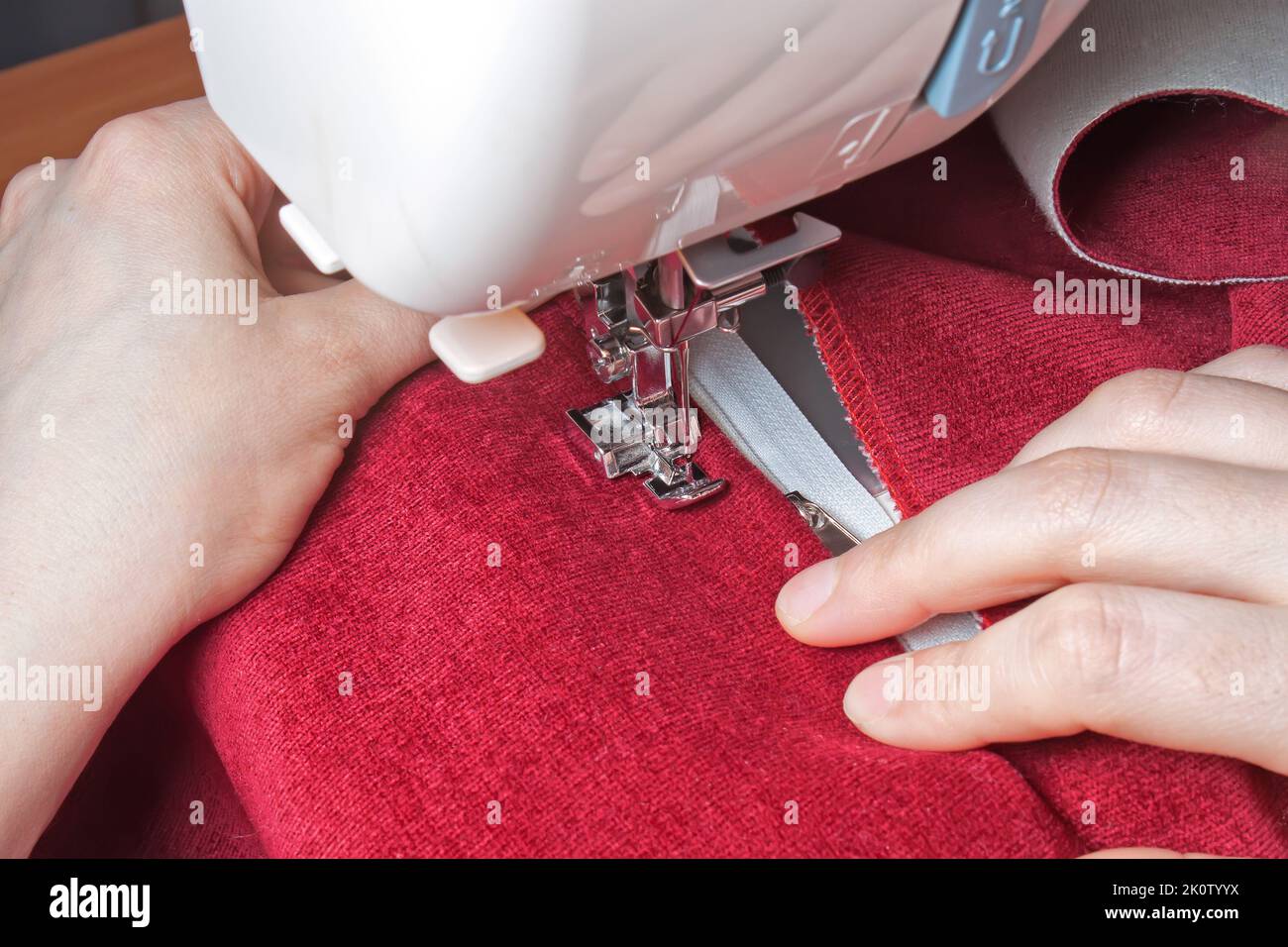 couturière les mains cousues sur la fermeture à glissière sur l'article rouge de vêtements par machine à coudre moderne avec le pied de presse spécial. processus de couture Banque D'Images