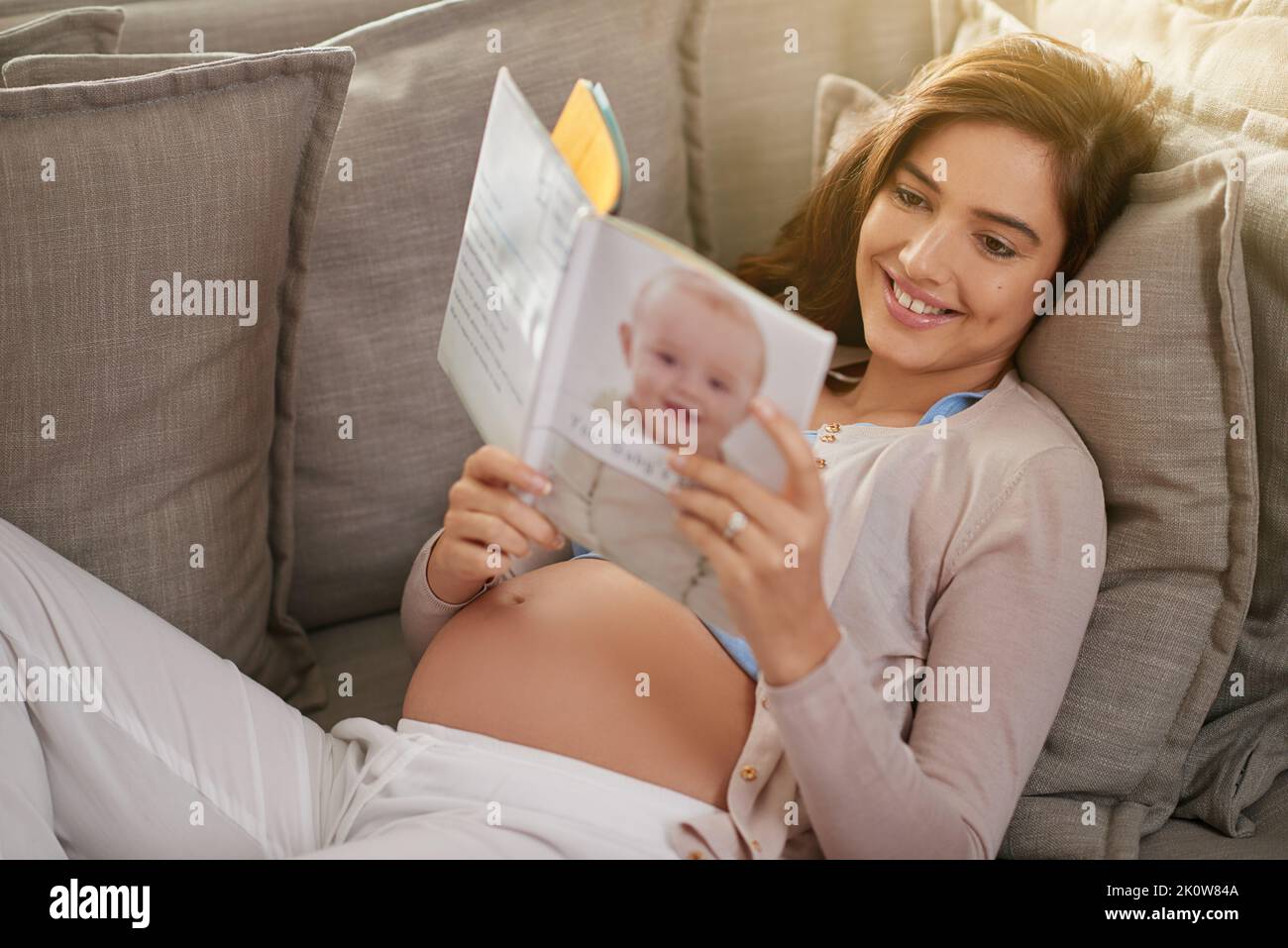 C'est le meilleur livre de bébé. Une jeune femme enceinte lisant un livre de bébé à la maison. Banque D'Images