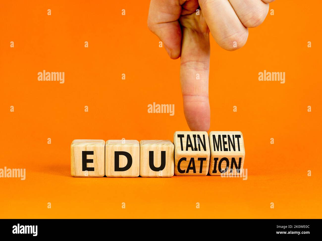 Symbole éducation et divertissement. Concept Words Education et edutainment sur des cubes en bois. Main du professeur. Belle table orange fond orange. EDU Banque D'Images