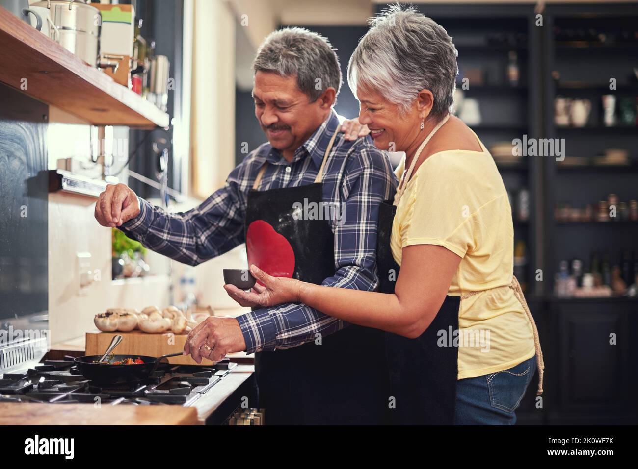 Juste une pincée de sel. Un heureux couple mature ajoutant du sel à un plat tout en cuisant ensemble à la maison. Banque D'Images