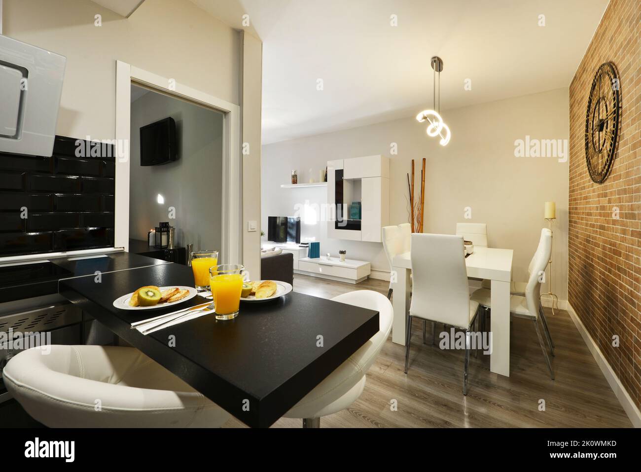 Petit appartement cuisine ouverte avec table en bois noir, tabourets blancs, mur décoratif en brique et table à manger en bois blanc Banque D'Images