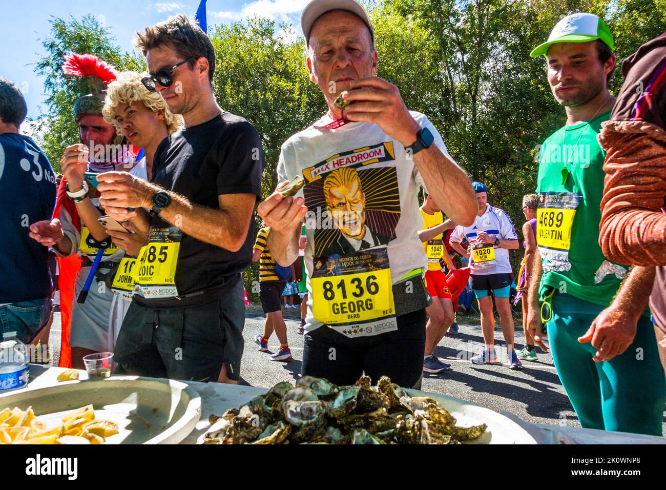 Pour le journaliste Georg Berg aussi, le stand d’huîtres près de l’arrivée du 36e Marathon des Châteaux du Médoc est le point culminant culinaire. De nombreux coureurs font ici une pause de plusieurs minutes pour profiter de cette spécialité de la région Nouvelle-Aquitaine. À côté de lui se tient un coureur portant un casque de légionnaire à plumes rouges. Pauillac, France. Banque D'Images