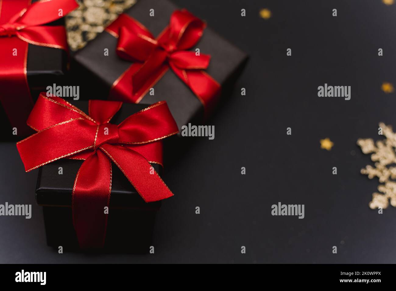 Boîtes-cadeaux noires avec ruban rouge sur fond de confettis dorés.Décor de Noël élégant avec décorations de Noël modernes dorées, boules, cadeau b Banque D'Images