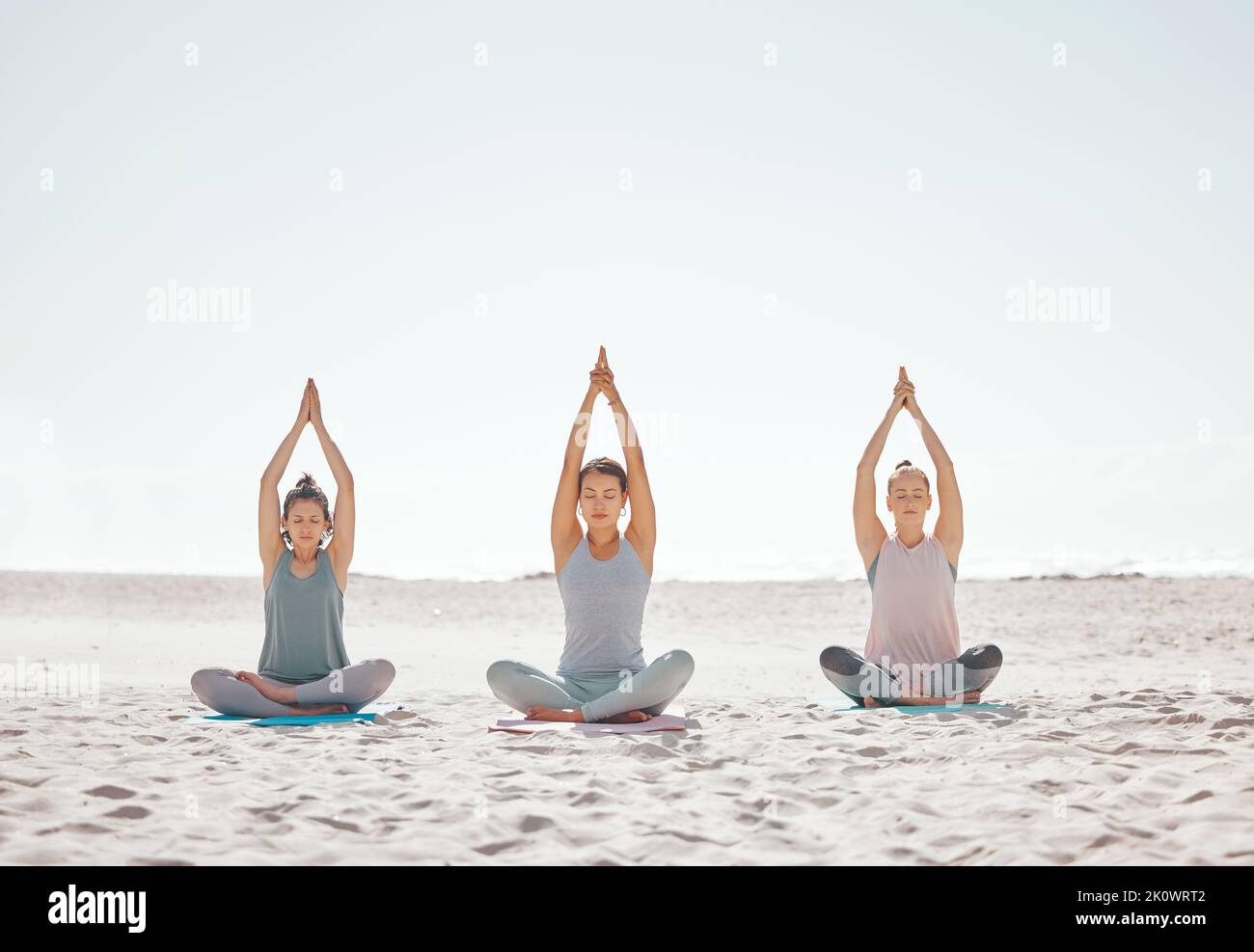 Zen, méditation et yoga à la plage avec des femmes pour le bien-être, la forme physique et la santé. Étirements, lotus pose et amis faisant un entraînement de pilates ou Banque D'Images