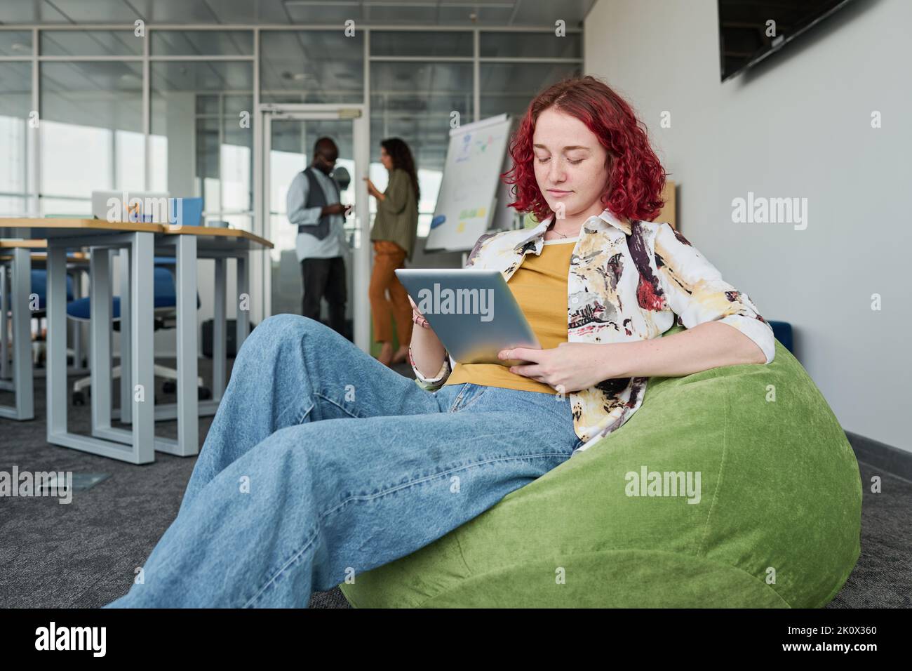 Jeune employé sérieux en tenue décontractée assis dans un fauteuil et en réseautage ou se préparant à une présentation au bureau Banque D'Images