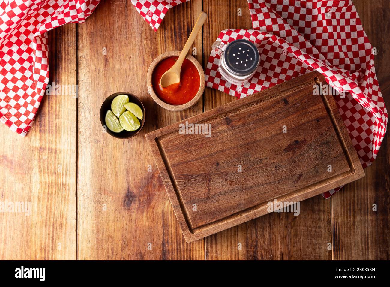 Fond de cuisson avec planche à découper vide avec citron, sauce mexicaine épicée au piment rouge et saupoudreuse sur table rustique en bois. Vue de dessus avec espace de copie Banque D'Images