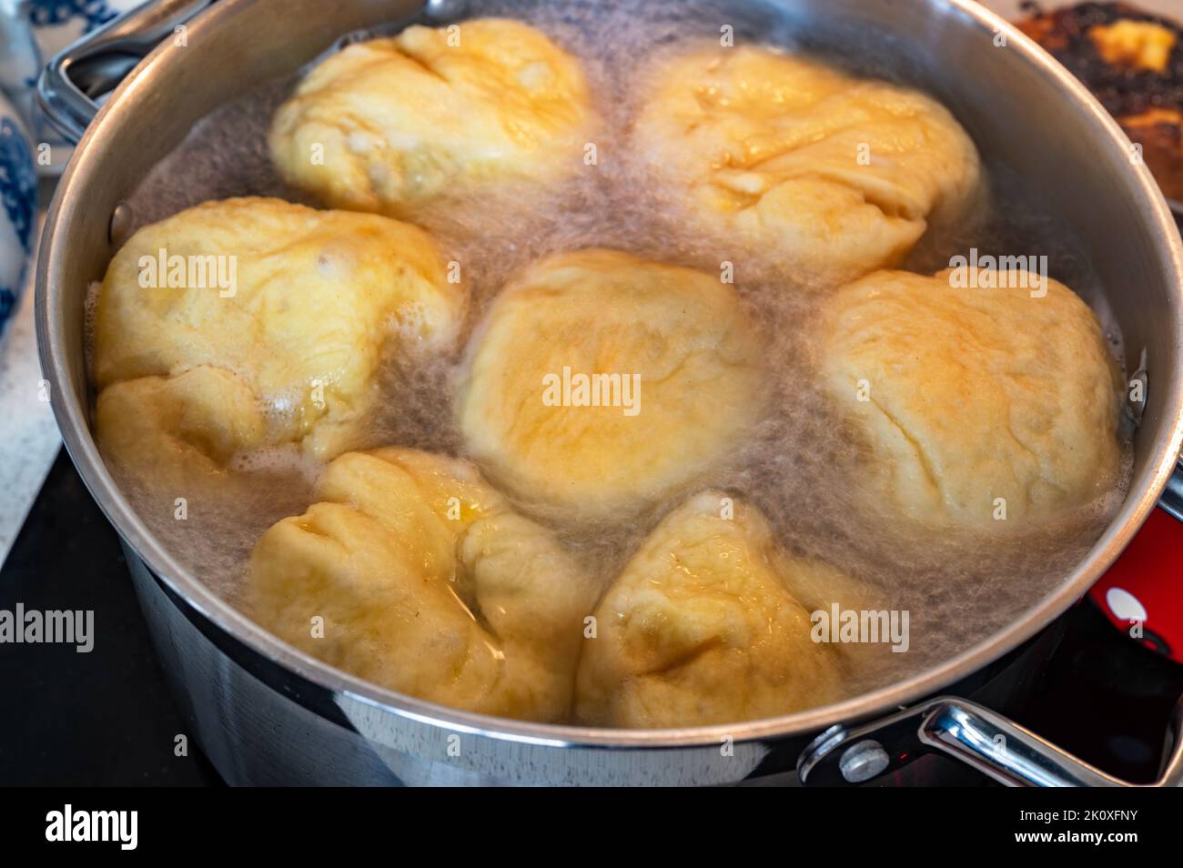 Faire bouillir le boulonnage dans une grande casserole. Boulettes de fruits doux flottant dans l'eau bouillante dans la casserole sur table de cuisson en céramique, gros plan. Préparation des aliments. Banque D'Images