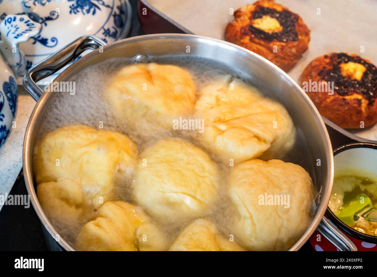 Boulettes de fruits doux flottant dans de l'eau bouillante dans une casserole sur une table de cuisson en céramique, beurre fondu dans une petite casserole, gâteau de 2 fti sur une table, gros plan. Préparation du boulonnage Banque D'Images