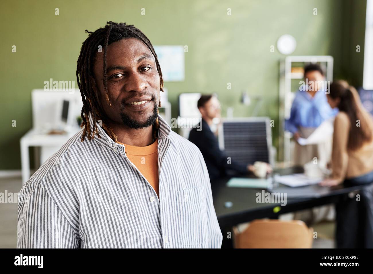 Portrait d'un homme africain souriant à la caméra tout en travaillant au bureau avec ses collègues Banque D'Images