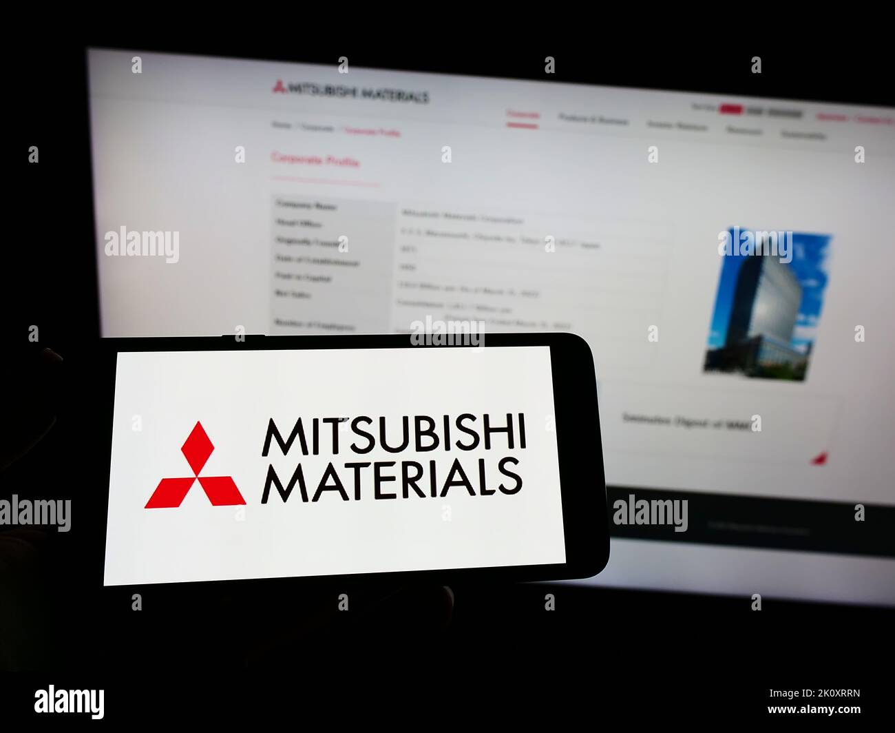 Personne détenant un smartphone avec le logo de la société Mitsubishi Materials Corporation (MMC) à l'écran devant le site Web. Mise au point sur l'affichage du téléphone. Banque D'Images