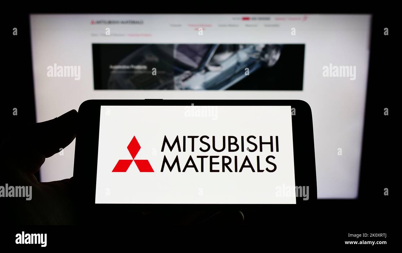 Personne tenant un téléphone portable portant le logo de la société Mitsubishi Materials Corporation (MMC) à l'écran devant la page Web. Mise au point sur l'affichage du téléphone. Banque D'Images