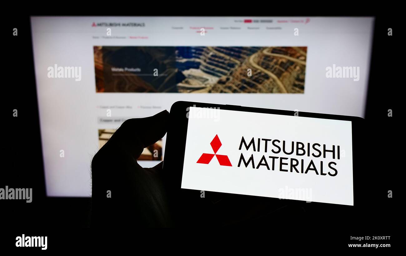 Personne tenant un téléphone portable portant le logo de la société Mitsubishi Materials Corporation (MMC) à l'écran devant la page Web. Mise au point sur l'affichage du téléphone. Banque D'Images