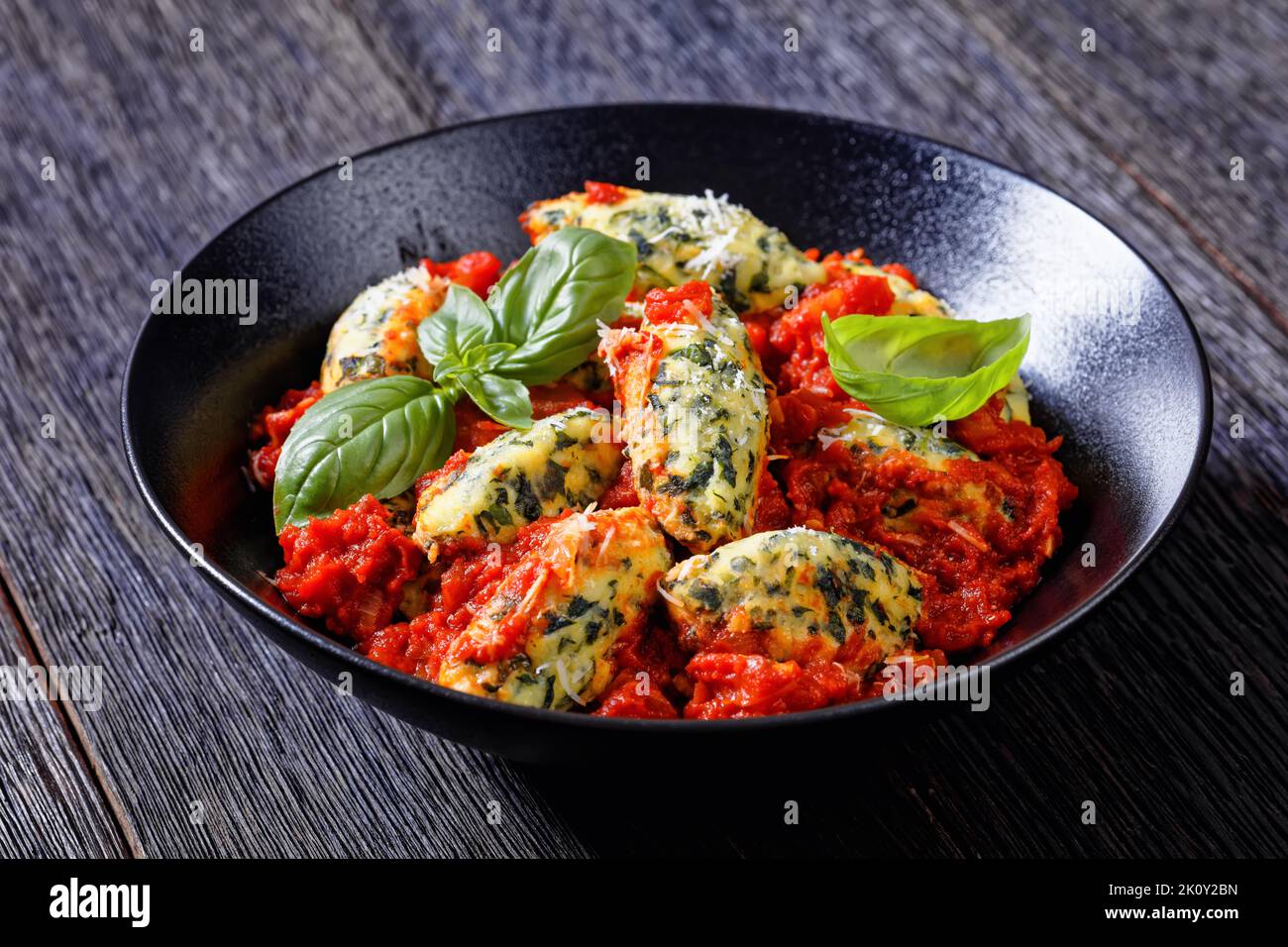 Boulettes de ricotta aux épinards italiens, sauce tomate aux herbes et parmesan râpé dans un bol noir sur une table en bois sombre Banque D'Images