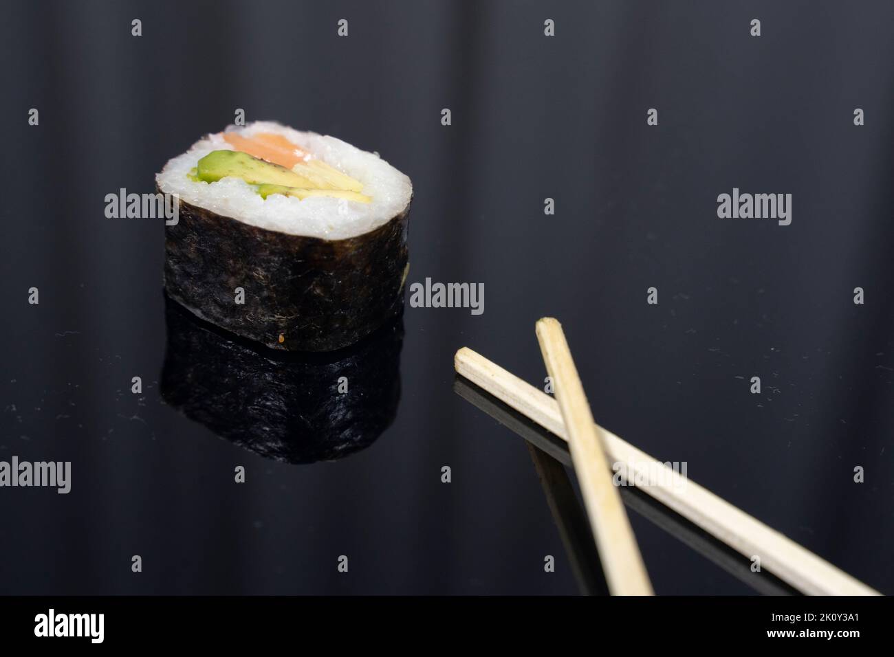 un morceau de sushi avec des baguettes sur fond sombre Banque D'Images