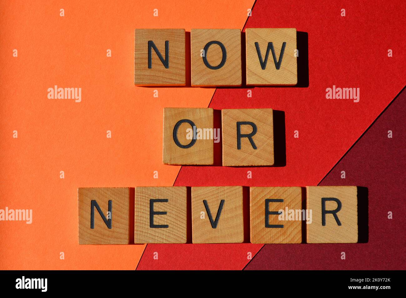 Maintenant ou jamais, les mots en lettres de l'alphabet de bois isolés sur fond rouge et orange Banque D'Images