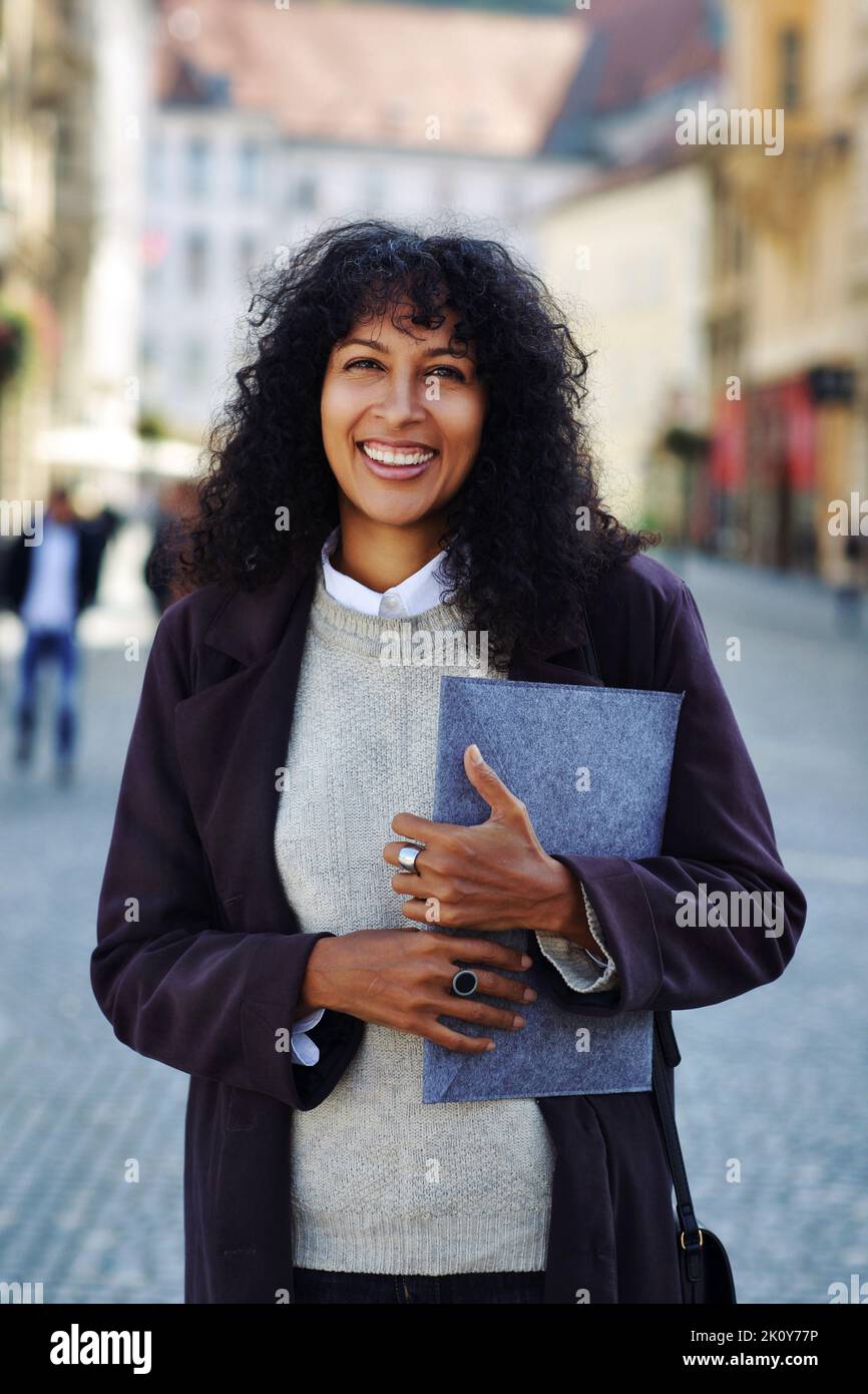 femme d'affaires positive debout dans la rue tenant une chemise avec des documents cheveux bouclés noirs Banque D'Images